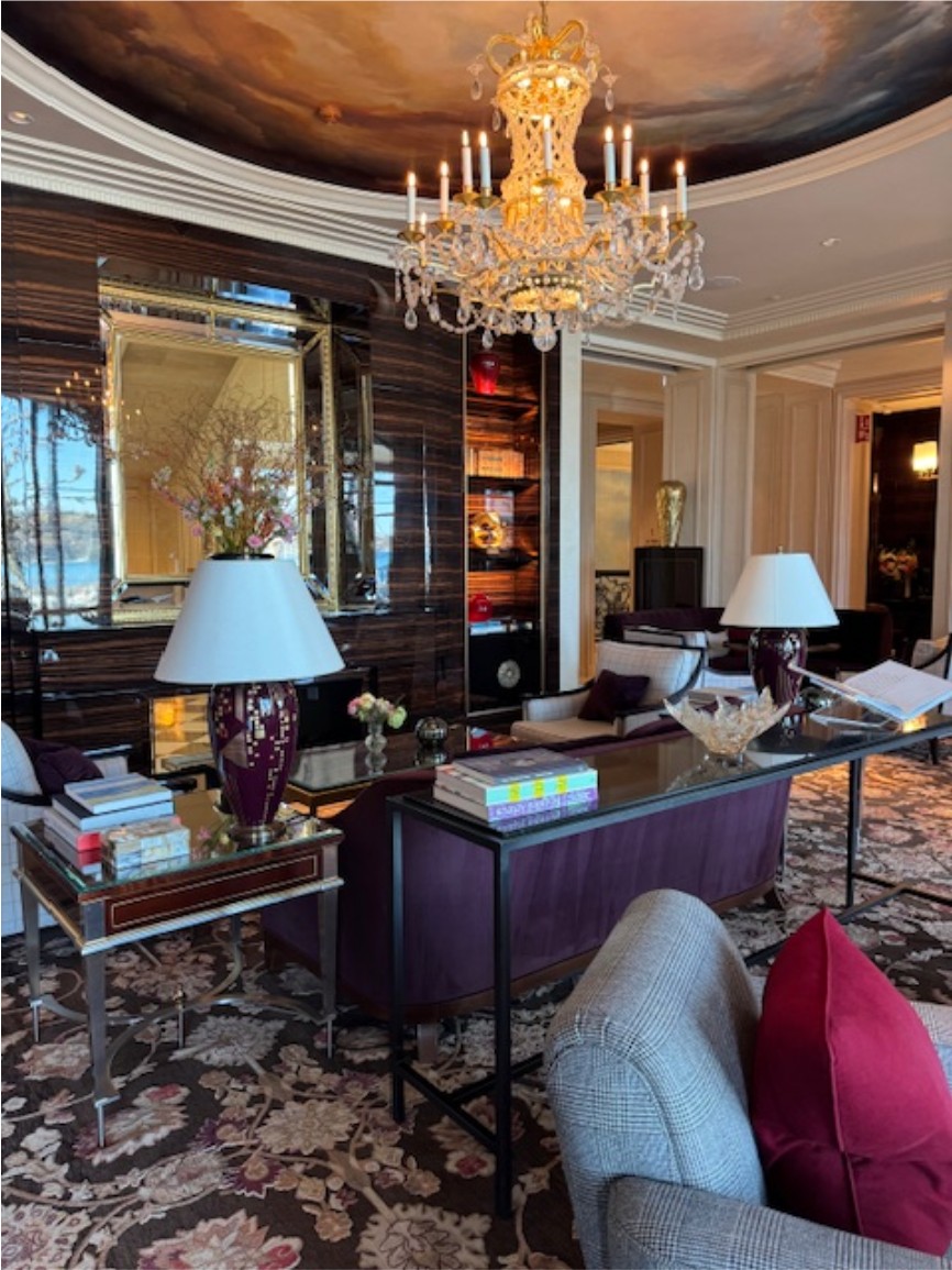 The lounge at The Woodward in Geneva, with a crystal chandelier, mahogany walls, and lake views.