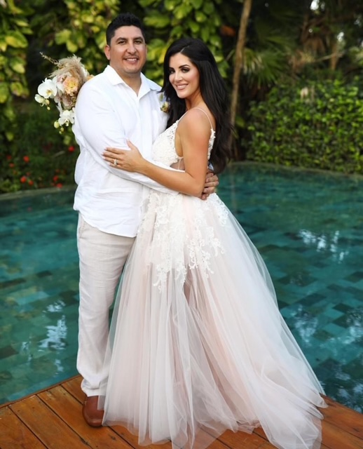 Newlyweds embracing beside a tropical pool with a bridal bouquet.
