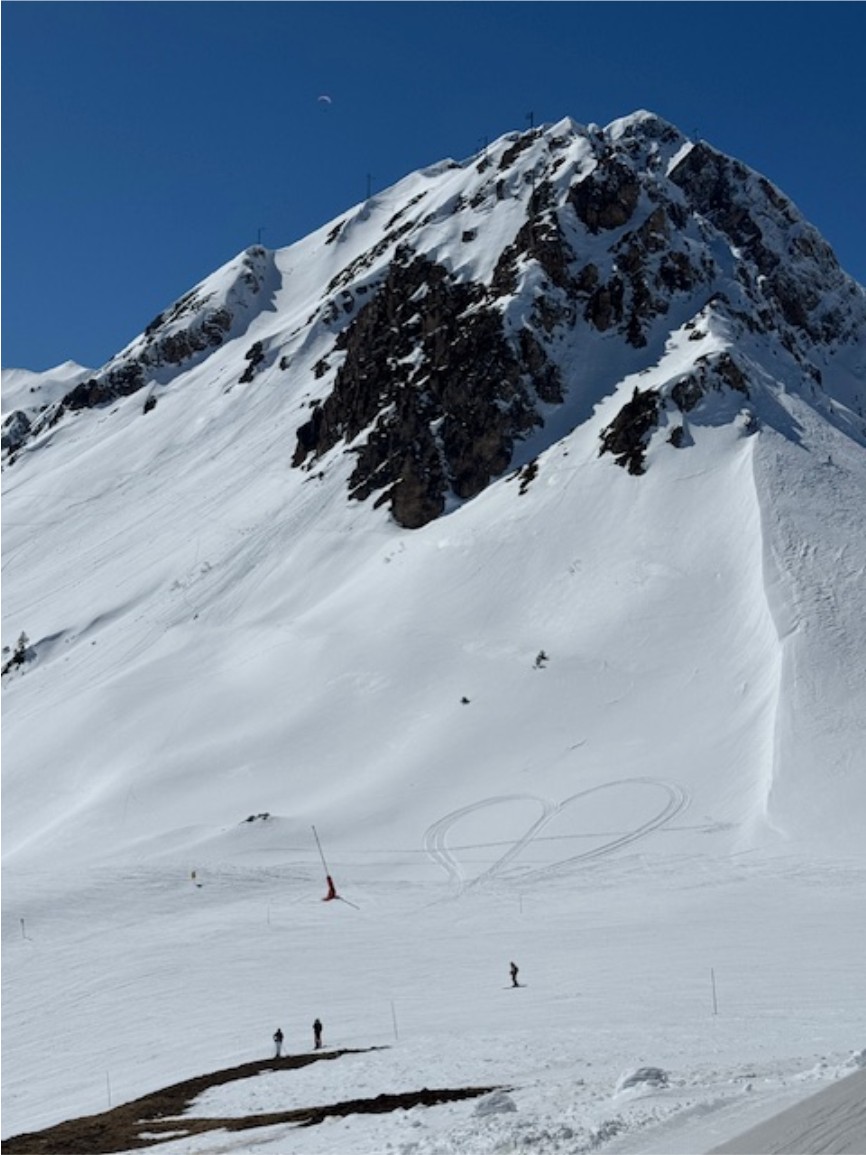 A snow-covered alpine peak in Courchevel under a clear blue sky, with a heart traced into the snow on the slope.