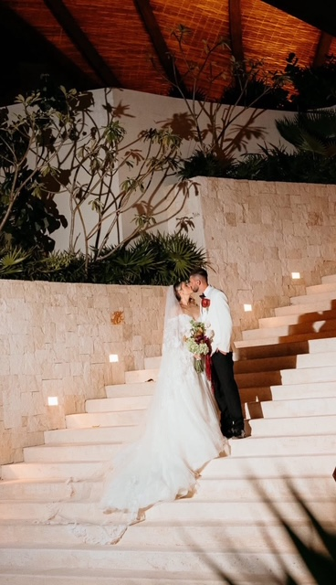 Bride and groom kissing on a candlelit stone staircase at a resort in the evening.